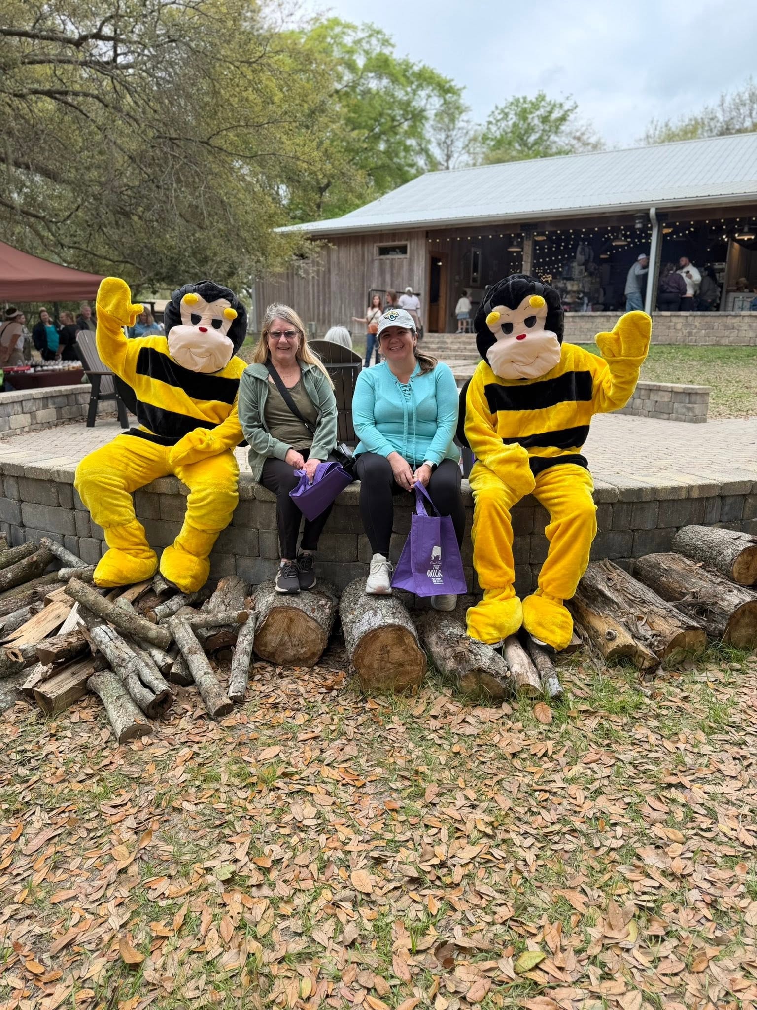 Two women sitting between AC Bee mascots at an outdoor community event